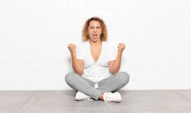 Orta yaşlı bir kadın sinirli bir ifadeyle ya da yumruklarıyla başarıyı kutlarken agresif bir şekilde bağırıyor.