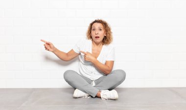 Orta yaşlı kadın şaşkın ve şaşırmış hissediyor. Kenardaki fotokopi alanını işaret ediyor. Şaşırmış ve ağzı açık bakıyor.