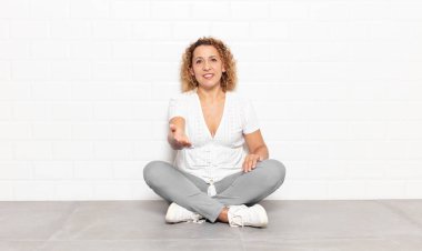 Orta yaşlı bir kadın gülümsüyor, mutlu, kendinden emin ve arkadaş canlısı görünüyor, bir anlaşmaya varmak için el sıkışmayı teklif ediyor, işbirliği yapıyor.