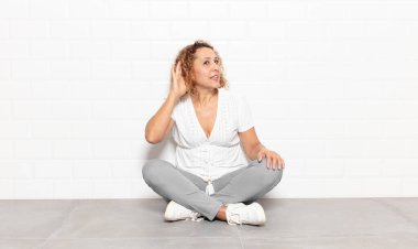 Orta yaşlı bir kadın ciddi ve meraklı görünüyor, dinliyor, gizli bir konuşma veya dedikodu duymaya çalışıyor, kulak misafiri oluyor.