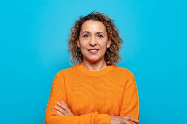 Kollarını kavuşturup kameraya gülümseyen orta yaşlı bir kadın ve mutlu, kendinden emin, tatmin olmuş bir ifade.