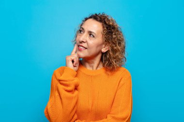 Orta yaşlı bir kadın mutlu bir şekilde gülümsüyor ve hayal kuruyor ya da şüphe ediyor.