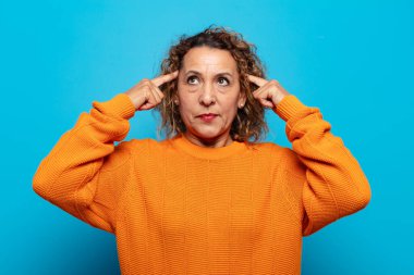 Orta yaşlı bir kadın kafası karışık ya da şüpheci, bir fikre odaklanmış, çok düşünüyor, kenarda boşluklar arıyor.