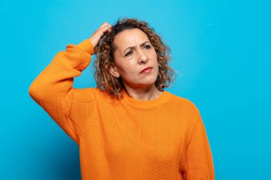 Orta yaşlı kadın şaşkın ve şaşkın hissediyor, kafasını kaşıyor ve yan tarafa bakıyor.