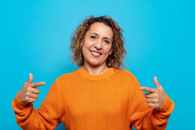 Orta yaşlı bir kadın gururlu, kibirli, mutlu, şaşırmış ve tatmin olmuş görünüyor.