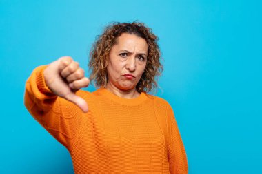 Orta yaşlı bir kadın sinirli, sinirli, hayal kırıklığına uğramış ya da canı sıkkın, ciddi bir bakışla başparmağını kaldırıyor.