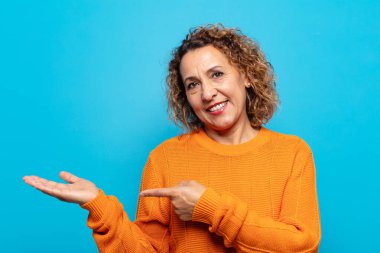 Orta yaşlı kadın gülümsüyor, mutlu, kaygısız ve tatmin olmuş hissediyor, fotokopi alanındaki konsepte veya fikre işaret ediyor.