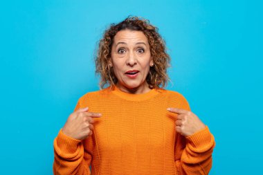 Orta yaşlı bir kadın mutlu, şaşkın ve gururlu hissediyor. Heyecanlı ve şaşkın bir bakışla kendini işaret ediyor.