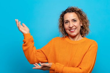 Orta yaşlı kadın gururla ve kendinden emin bir şekilde gülümsüyor, mutlu ve tatmin olmuş hissediyor ve fotokopi alanında bir konsept gösteriyor.