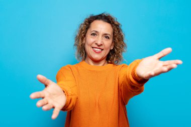 Orta yaşlı bir kadın neşeyle gülümsüyor sıcak, dostça, sevgi dolu bir kucak veriyor, mutlu ve sevimli hissediyor.