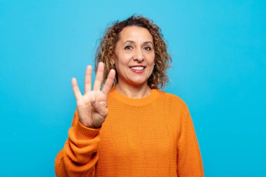 Orta yaşlı bir kadın gülümsüyor ve arkadaş canlısı görünüyor. Elleri önde, geriye doğru sayıyor.