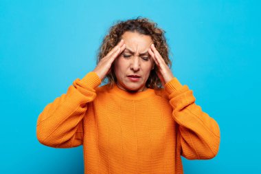 Stresli ve hayal kırıklığına uğramış görünen orta yaşlı bir kadın, baskı altında çalışıyor, başı ağrıyor ve sorunları var.