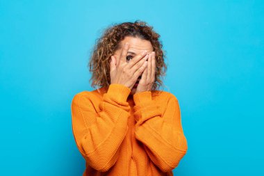 Orta yaşlı bir kadın korkmuş ya da utanmış hisseder. Gözleri yarı kapalı, yarı çıplak bir şekilde dikizler ya da gözetler.