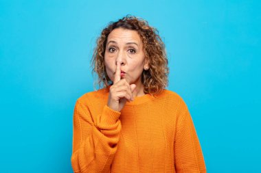 Orta yaşlı bir kadın sessizlik ve sessizlik istiyor, parmağıyla ağzının önünde işaret ediyor, 