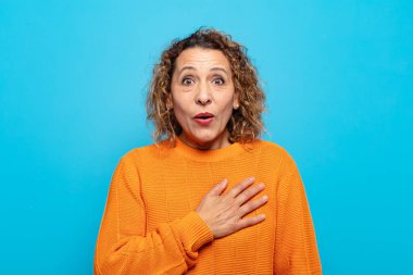 Orta yaşlı bir kadın şaşkın ve şaşırmış hissediyor, gülümsüyor, el ele tutuşuyor, o olmaktan mutlu ya da minnettarlık gösteriyor.