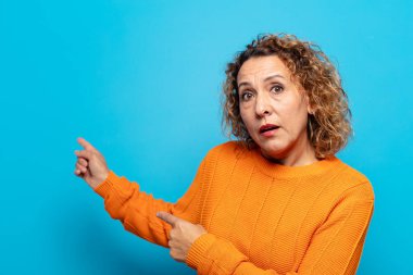 Orta yaşlı kadın şaşkın ve şaşırmış hissediyor. Kenardaki fotokopi alanını işaret ediyor. Şaşırmış ve ağzı açık bakıyor.