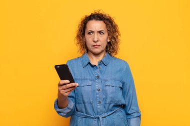 Hispanik orta yaşlı kadın üzgün, üzgün ya da kızgın hissediyor ve olumsuz bir tutumla yan yana bakıyor, anlaşmazlık içinde kaşlarını çatıyor