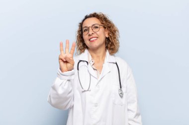 İspanyol orta yaşlı kadın gülümsüyor ve arkadaş canlısı görünüyor. Üç ya da üç numarayı gösteriyor. Elleri önde, geriye doğru sayıyor.