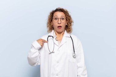 İspanyol orta yaşlı kadın şok olmuş ve şaşırmış görünüyor ağzı açık, kendini işaret ediyor.