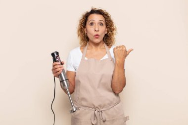 İspanyol orta yaşlı kadın inançsızlıktan şaşkın şaşkın bakıyor, yan taraftaki objeyi işaret ediyor ve diyor ki: