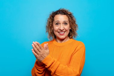 Orta yaşlı kadın mutlu ve başarılı hissediyor, gülümsüyor ve alkışlıyor, alkışlarla tebrik ediyor.