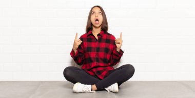 İspanyol kadın şaşırmış, şaşırmış ve ağzı açık bakıyor, iki eliyle uzayı işaret ediyor.