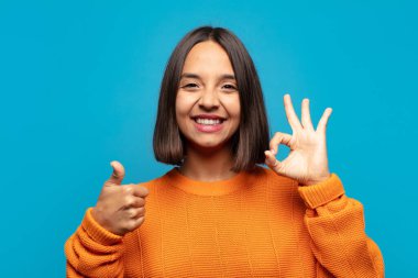 İspanyol kadın kendini mutlu, şaşkın, tatmin olmuş ve şaşırmış hissediyor, iyi olduğunu gösteriyor ve el kol hareketleri yapıyor, gülümsüyor.