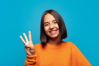 İspanyol kadın gülümsüyor ve arkadaş canlısı görünüyor. Üç ya da üç numarayı gösteriyor. Elleri önde, geri sayıyor.