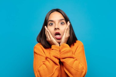 İspanyol kadın şok olmuş ve korkmuş hissediyor, ağzı açık ve elleri yanaklarında korkmuş görünüyor.