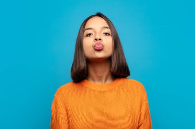 Tatlı, eğlenceli, mutlu, sevimli bir yüz ifadesiyle dudaklarını birbirine bastıran İspanyol kadın öpücük yolluyor.