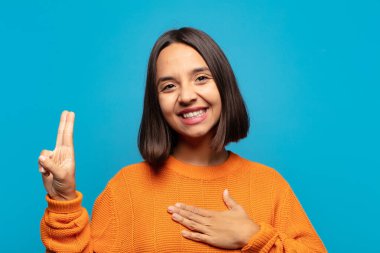 İspanyol kadın mutlu, kendinden emin ve güvenilir görünüyor, gülümsüyor ve zafer işareti gösteriyor, olumlu bir tavırla.