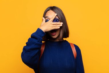 İspanyol kadın şok olmuş, korkmuş ya da korkmuş görünüyor. Yüzü elle kaplanmış ve parmaklarının arasından gizlice bakıyor.