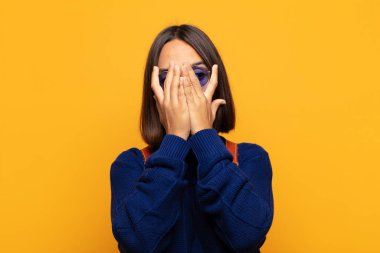 İspanyol kadın elleriyle yüzünü kapatıyor, parmaklarının arasından şaşkın bir ifadeyle yan tarafa bakıyor.