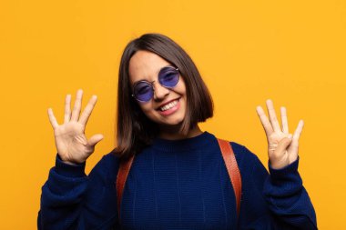 İspanyol kadın gülümsüyor ve arkadaş canlısı görünüyor, 9 ya da 9 numarayı gösteriyor, eli önde, geri sayıyor.