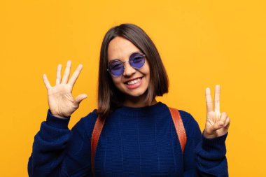 İspanyol kadın gülümsüyor ve arkadaş canlısı görünüyor, 7 ya da 7 numarayı gösteriyor, eli önde, geriye doğru sayıyor.