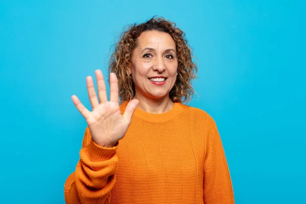 Orta yaşlı bir kadın gülümsüyor ve arkadaş canlısı görünüyor. 5 ya da 5 numarayı gösteriyor.