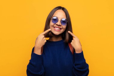 İspanyol kadın kendine güvenerek gülümsüyor. Kendi gülüşünü gösteriyor. Olumlu, rahat, tatmin olmuş tavır.