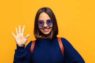 İspanyol kadın gülümsüyor ve arkadaş canlısı görünüyor, 5 ya da 5 numarayı gösteriyor, elleri önde, geri sayıyor.