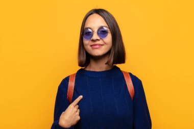 İspanyol kadın gururlu, kendinden emin ve mutlu görünüyor, gülümsüyor ve kendini işaret ediyor ya da bir numara işareti yapıyor.