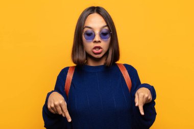 İki eliyle aşağıya bakan ağzı açık İspanyol bir kadın. Şok olmuş, şaşırmış ve şaşırmış görünüyor.