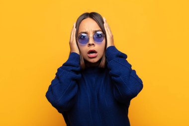 İspanyol kadın hoş olmayan bir şekilde şok olmuş, korkmuş ya da endişeli görünüyor, ağzı sonuna kadar açık ve iki kulağını da elleriyle kapatıyor.