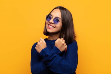 İspanyol kadın sevinçle gülümsüyor ve kutluyor, yumruklarını sıkmış ve kollarını kavuşturmuş, mutlu ve pozitif hissediyor.