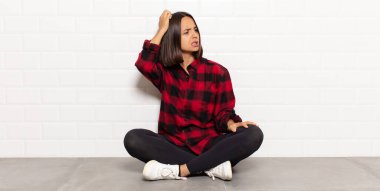 İspanyol kadın şaşkın ve şaşkın hissediyor, kafasını kaşıyor ve yan tarafa bakıyor.