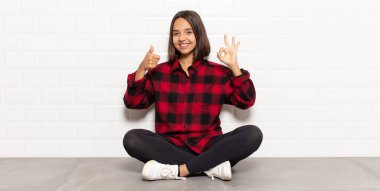 İspanyol kadın kendini mutlu, şaşkın, tatmin olmuş ve şaşırmış hissediyor, iyi olduğunu gösteriyor ve el kol hareketleri yapıyor, gülümsüyor.