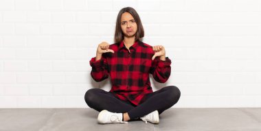 Hispanik kadın üzgün, hayal kırıklığına uğramış ya da kızgın görünüyor, anlaşmazlık içinde başparmaklarını gösteriyor, hayal kırıklığına uğramış hissediyor