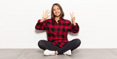 İspanyol kadın gülümsüyor ve arkadaş canlısı görünüyor, 7 ya da 7 numarayı gösteriyor, eli önde, geriye doğru sayıyor.