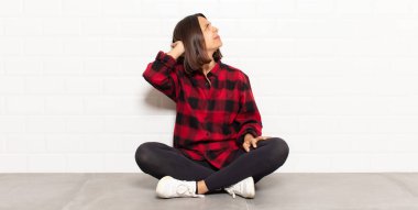 Hispanik kadın düşünüyor ya da şüphe ediyor, kafasını kaşıyor, şaşkın ve şaşkın hissediyor, arkaya ya da arkaya bakıyor.