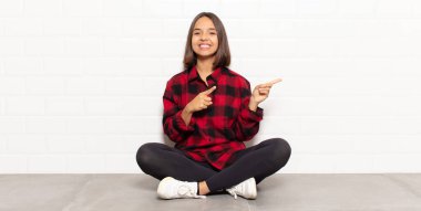 İspanyol kadın mutlu bir şekilde gülümsüyor ve her iki elini de fotokopi alanında objeler gösteriyor.