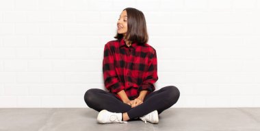 İspanyol kadın neşeyle gülümsüyor, mutlu, tatmin olmuş ve rahatlamış hissediyor, kollarını kavuşturup yan tarafa bakıyor.