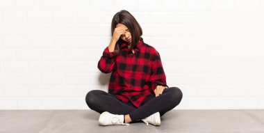 İspanyol kadın stresli, utanmış ya da üzgün görünüyor, baş ağrısı var, yüzünü elleriyle kapatıyor.